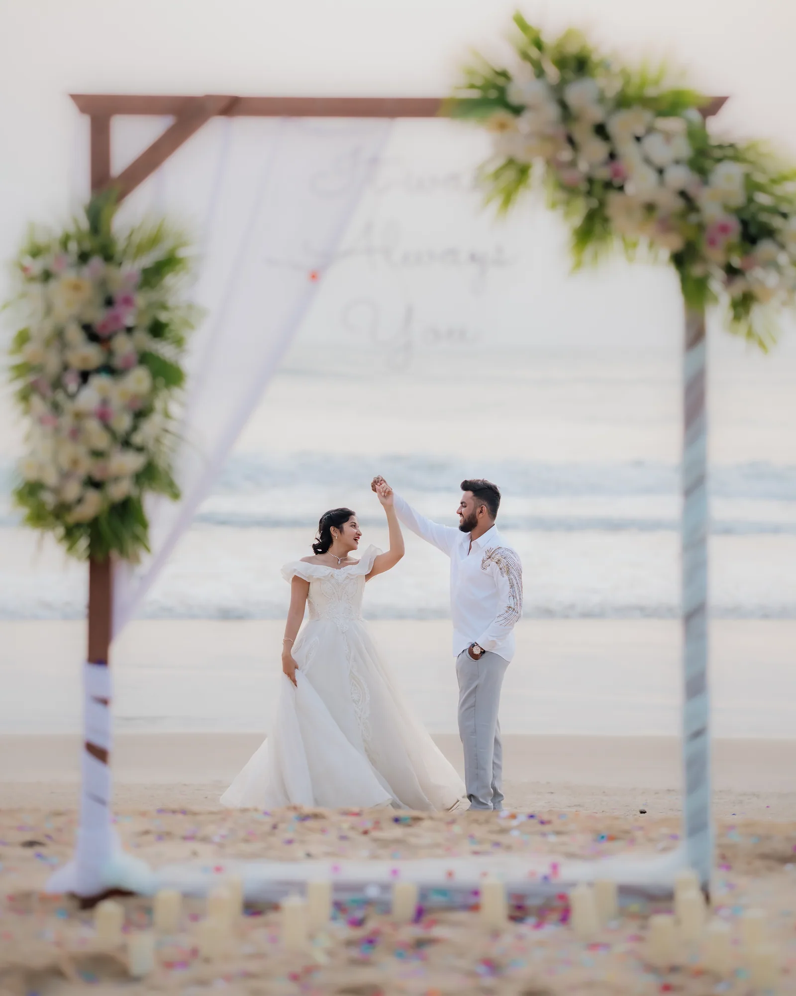 A couple dancing under a flower arch by the sea, photographed by Darshan Ravi Photography